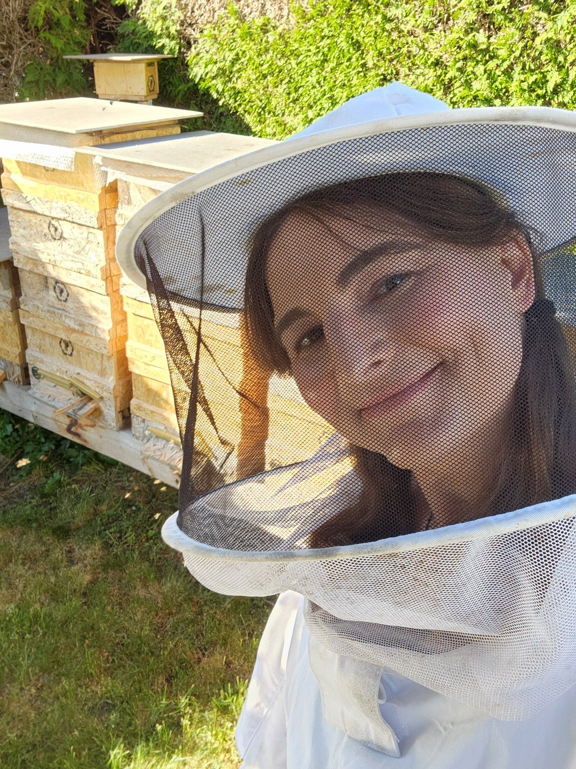 Diana S. Engelhard wearing a beekeeper veil beside beehives.