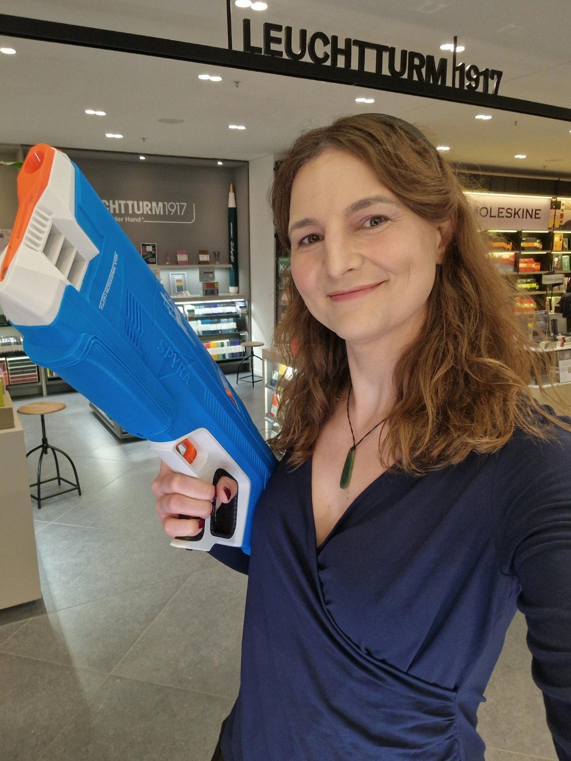 Diana S. Engelhard holding an oversized blue toy blaster in a stationery shop.